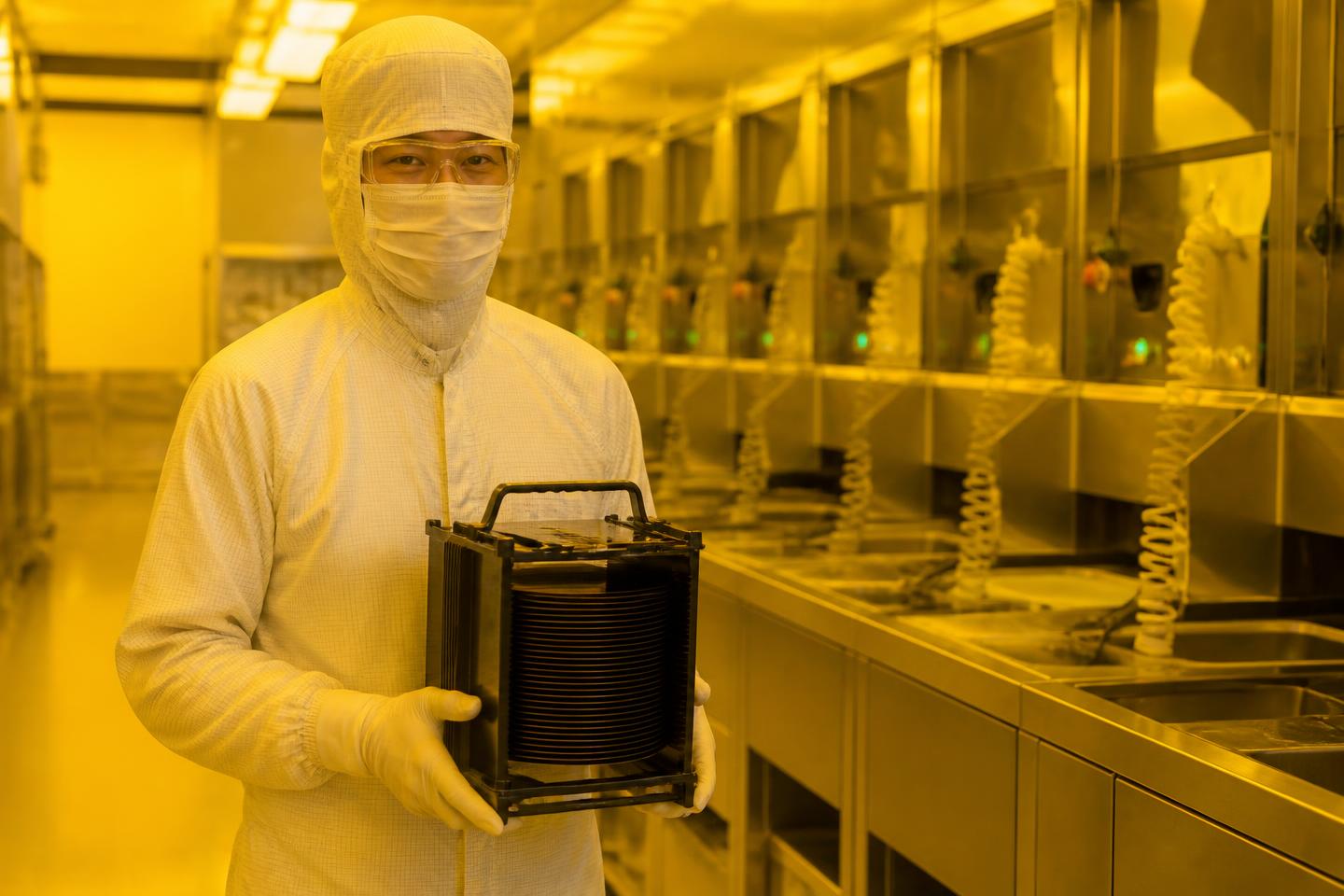 Process engineer inspecting a 300 mm wafer carrier under yellow cleanroom light at a microLED fab near Grenoble, wet-bench station in the background.