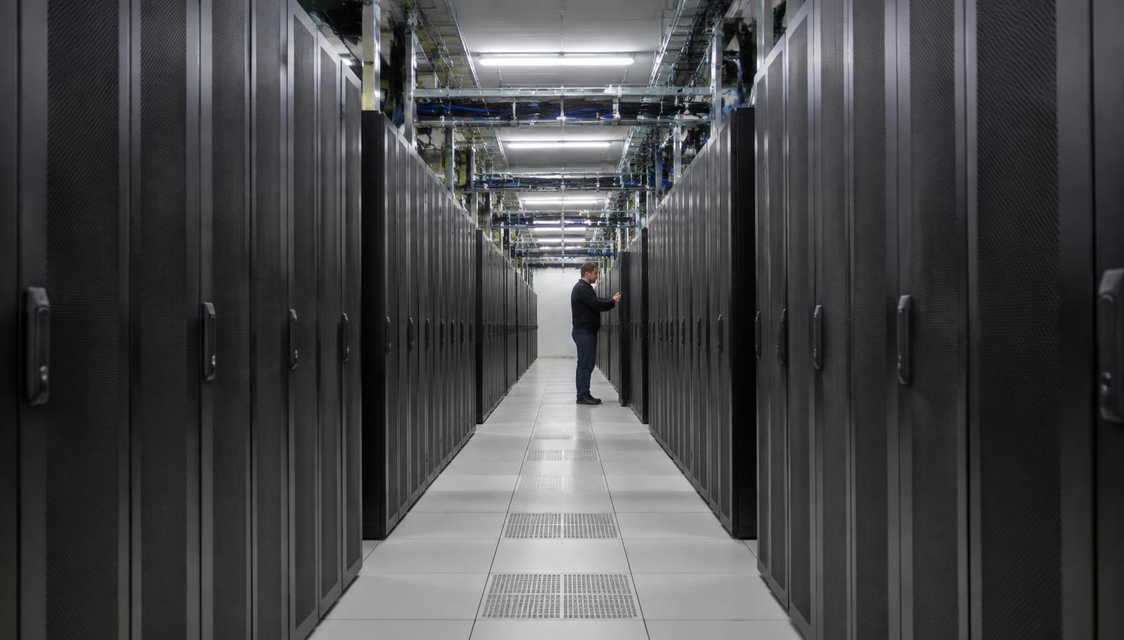 Un ingénieur vérifie une baie dans une longue allée de supercalculateurs noirs, dans la salle machine d'un centre de calcul national